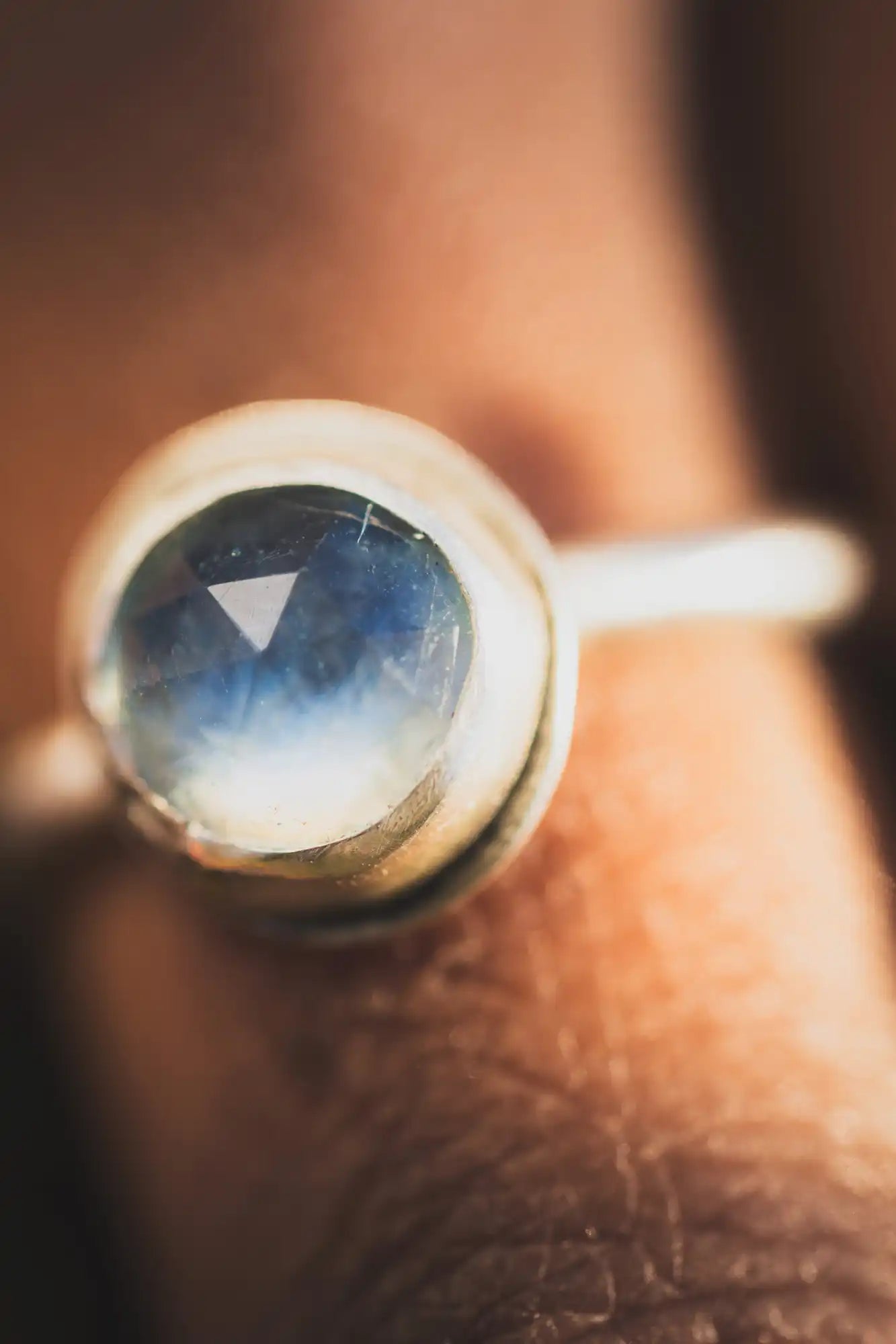 Anillo de oro con una gema de piedra de luna redonda que tiene un brillo azul-blanco.