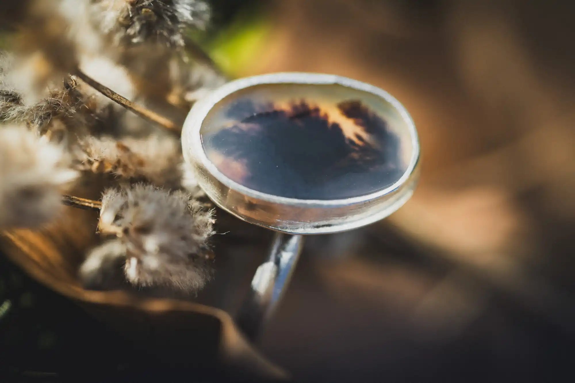 Un anillo de plata que refleja el cielo y las nubes en su superficie.